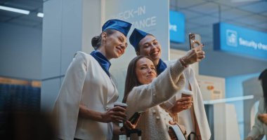 Zarif üniformalı iki güzel uçuş görevlisi konuşuyor, ticari uçuşu bekliyor. Kabin Ekibi 'ne gelen, Selfie çeken bir kadın. Kalabalık Uluslararası Havaalanı Terminali. Yavaş Hareket.