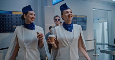 Kalabalık Uluslararası Havaalanı Terminali: Arkalarında Profesyonel Havayolu Pilotu ile Zarif Üniformalı İki Güzel Uçuş Görevlisi Konuşuyor, Ticari Uçuş İçin Yürüyor. Yavaş Hareket.