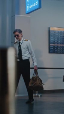 Havaalanı Terminali: Olgun Havayolu Pilotu ve Zarif Üniformalı İki Güzel Uçuş Görevlisi, Uçak Uçuşu için Bavulla Yürüyorlar, Bayan Güvenlik Subayının yanından geçiyoruz. Dikey Çekim.