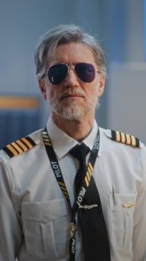 Gözlüklü ve üniformalı, Kameraya Bakan Profesyonel Havayolu Yüzbaşısının Portresi. Uluslararası Havalimanı Terminali 'nde Uçuş Ekibi Üyesi ve Arka planda Yolcular. Orta derecede yakın çekim. Dikey Çekim.