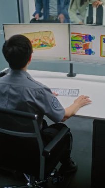 Havaalanı Güvenlik Kontrol Noktası: Modern Yazılım Kullanılarak Bavul Bilgisayar Ekranlarında Kadın Güvenlik Görevlisi X-ray taraması yapıyor. Gösterim sırasında çeşitli bagajlı gezginler. Dikey Çekim.