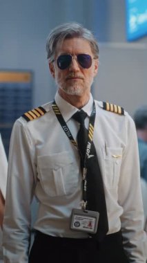 Profesyonel Hava Yolları Pilotu ve Üniformalı İki Uçuş Görevlisi Gülümseyen, Kameraya Bakan Portresi. Kalabalık Uluslararası Havaalanı Terminalinde Uçuş Ekibi Üyeleri. Orta boy shot. Dikey Çekim.