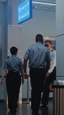 Kalabalık Uluslararası Havaalanı Terminali 'nde bavullu çeşitli yolcular. Uçak Pilotu ve Bavullu İki Uçuş Görevlisi Güvenlik Kontrol Noktasından Uçak Yürüyüşü Geçiyorlardı. Dikey Çekim