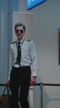 Havaalanı Terminali: Havaalanı Kaptanı, İki Güzel Hostes Ticari Uçuş için Bavullarıyla Yürüyor, Güvenlik Kontrol Noktasından Bayan TSA memurunun yanından geçiyor. Ağır çekim. Dikey Çekim