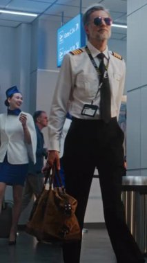 Kalabalık Uluslararası Havaalanı Terminali: Havayolu Yüzbaşısı ve iki güzel hostes Ticari Uçuş Bavullarıyla Yürüyor, Güvenlik Kontrol Noktasını Geçiyor. Ağır çekim. Dikey Çekim