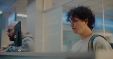 Havaalanı check-in gişesindeki çeşitli yolcular: Uluslararası Havalimanı Terminali 'nde Kimlik Verisini Yüz Tanıma Taramasıyla Doğrulayan, Pasaport Kontrolü sırasında Havayolu İşçisiyle Konuşan Genç Adam.