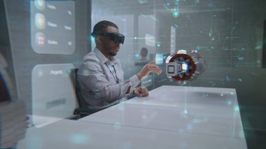 Geleceğin Ofisi: Yeşil Enerji Motorunun 3 boyutlu holografik prototipini görüntülemek için Sanal Gerçeklik Kulaklığı takan Afro-Amerikan Profesyonel Ofisi. Yapay Zeka tabanlı arayüzün görselleştirilmesi.