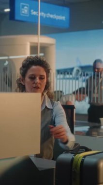 Havaalanı sayacındaki çeşitli yolcular: Kadın Havayolu check-in görevlisi Erkek Bagajını kontrol ediyor, Uçuş Bavuluna Barkod etiketi koyuyor. Havaalanı terminalindeki güvenlik kontrol noktası. Dikey Çekim.