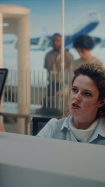 Havaalanı kontrol gişesi: Kadın havayolu işçisi, uçuş için kişisel kimlik bilgilerini kontrol ediyor. Biyometrik Parmak izi taraması için Dokunmatik Ekrana Parmak Koyan Adam. Havaalanı Terminali. Dikey Çekim.