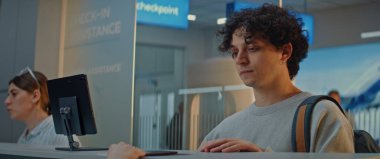 Havaalanı kontrol gişesi: Genç Adam Yüz Tanıma Taramasından Kimliğini Onayladı, Kadın Havayolu Ajanı Uçuş Yolcusunun Biyometrik Verilerini Kontrol Etti. Havaalanı terminalinde pasaport kontrolü. Yavaş Hareket.