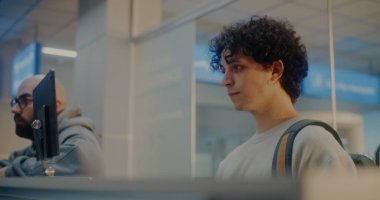 Havaalanı check-in gişesindeki çeşitli yolcular: Uluslararası Havalimanı Terminali 'nde Kimlik Verisini Yüz Tanıma Taramasıyla Doğrulayan, Pasaport Kontrolü sırasında Havayolu İşçisiyle Konuşan Genç Adam.