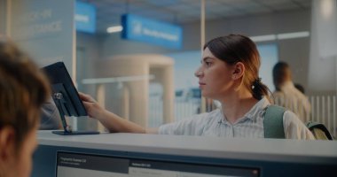 Havaalanı kontrol gişesi: Parmak izi taraması yapan yolcu. Bayan Havayolu İşçisi Bilgisayarda Kişisel Kimlik Verilerini Kontrol Ediyor, Belgeler Veriyor ve Kadına Giriş Kartı Veriyor. Uluslararası Havaalanı Terminali