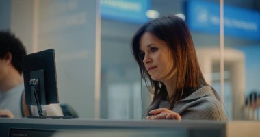 Havaalanı check-in gişesindeki çeşitli yolcular: Havayolu çalışanıyla konuşan kadının yakın çekimi, uçuş için pasaport kontrolü bekleniyor. Uluslararası Havaalanı Terminalinde Sınır Kontrolü.