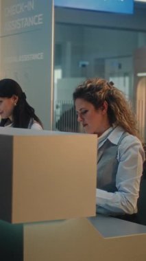 Uluslararası Havalimanı Terminali: Genç Erkek Yolcu Bavulu, Uçuş öncesi Bagaj Bildirimi için Tezgahı yakınında, Bayan Havayolu Ajanıyla Konuşuyor. Güvenlik kontrol noktası. Dikey Çekim.