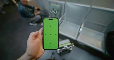 Kalabalık Havalimanı Terminali: POV Man, Airline Hub Lounge 'da duruyor, Smartphone Green Chroma Key Mockup ile kayıyor. Sosyal Medya İçeriği için Yer Tutucu ile Görüntü Şablonu. İlk Kişi Görünümü.