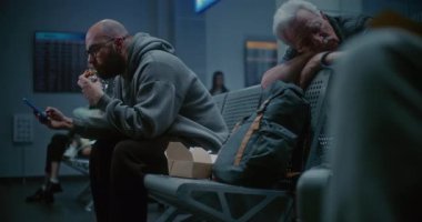 Gece Havayolları İnbotu Biniş Salonu: İnsan Fast Food yiyor ve Uluslararası Kalabalık Havaalanı Terminalinde Akıllı Telefon Kullanıyor. Yorgun Yolcular ve Gezginler Gecikmiş Uçak Uçuşunu Bekliyor