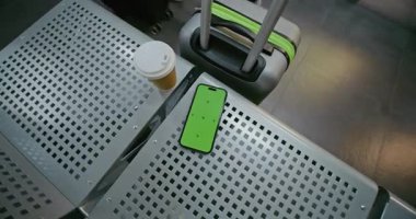Havaalanı Terminalindeki Havayolu Hub Lounge: Yeşil Kroma Anahtarlı Akıllı Telefon Mockup Kahve ve Bavul 'un yanındaki koltukta uzanıyor. Sosyal Medya İçeriği için Yer Tutucu ile Görüntü Şablonu. El bilgisayarı.