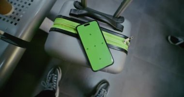 Kalabalık Uluslararası Havaalanı Terminali: Yeşil Kroma Anahtarlı Akıllı Telefon Bavulun Üzerinde Uzanıyor. İş Dünyası Reklamcılığı ve Sosyal Medya İçeriği için Video Şablonu. El bilgisayarı.