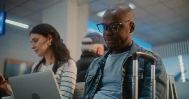 Kalabalık Uluslararası Havalimanı Terminali: Laptop 'ta Uzaktan Çalışan Afrikalı Amerikalı Girişimci, Telefonu Kullanıyor. Uçağı bekleyen çeşitli yolcular, havayolu merkezinin biniş salonunda oturuyorlar..