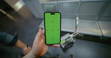 Kalabalık Havalimanı Terminali: POV Adam Yeşil Krom Anahtarlı Cep Telefonu ile Ayrılış Salonunda Bekliyor. İş Reklamcılığı için Yer Tutucu ile Görüntü Şablonu. İlk Kişi Görünümü.