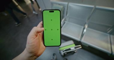 Kalabalık Havaalanı Terminali: Man Standing in Airline Hub Lounge, Holding Mobile Phone with Green Chroma Key Moplay Mock Up. İş Reklamcılığı için Yer Tutucu ile Görüntü Şablonu. İlk Kişi Görünümü.