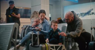 Kalabalık Havaalanı Terminalinde Uçağı Bekleyen Çocuklu Aile. Kadın Bebekle Oynuyor, Erkek, Küçük Oğlu ile Dijital Tablet 'te Çizgi Film İzliyor. Airlines Hub Lounge 'da Çeşitli İnsanlar.