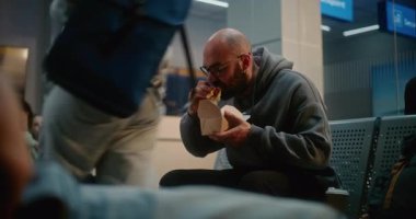 Kalabalık Uluslararası Havaalanı Terminali: Fast Food Yiyen Adam Havayolu Merkezinin Gidiş Salonunda Oturuyor. Çeşitli Yolcular ve Gezginler Gecikmiş Uçak Uçuşunu Bekliyor, Tatile Çıkıyor.