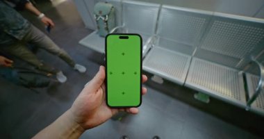 Kalabalık Havalimanı Terminali: POV Adam Havalimanı Hub Lounge 'da duruyor, Akıllı Telefonu Yeşil Kroma Anahtarlı Ekran Moklavyesi ile tutuyor. Sosyal Medya İçeriği için Yer Tutucu ile Görüntü Şablonu. İlk Kişi Görünümü.