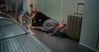 Kalabalık Uluslararası Havalimanı Terminali: Yorgun Adam Havayolu Merkezinin Yatılı Salonu 'ndaki Bavul' un yakınında uyuyor. Çeşitli yolcular rötarlı uçuş bekliyor. Turizm ve Seyahat. El bilgisayarı
