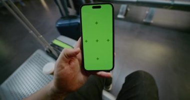 Kalabalık Havalimanı Terminali: POV Adam Havayolu Hub Lounge 'da oturuyor, Smartphone Green Chroma Key Mockup ile kayıyor. Sosyal Medya İçeriği için Yer Tutucu ile Görüntü Şablonu. İlk Kişi Görünümü.