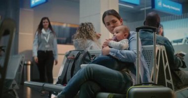 Kalabalık Uluslararası Havaalanı Terminali: Yetişkin Kadın Bebek Oturuyor ve Uçak Bekliyor. Kadın havaalanı işçisi, kadınla konuşuyor. Hava Yolları Merkezinin Ayrılış Salonundaki Çeşitli Yolcular.