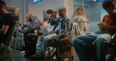 Kalabalık Uluslararası Havaalanı Terminali: Airline Hub 'ın Kalkış Salonunda oturan çeşitli Yolcular, Uçak Uçuşunu Bekliyor, Telefonları Kullanıyor. Laptop 'ta Uzaktan Çalışan Afrikalı Amerikalı Adam.