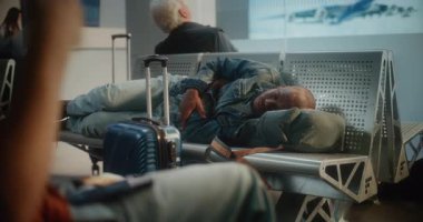 Kalabalık Uluslararası Havalimanı Terminali: Yorgun Afrikalı Amerikalı Adam ve Uçak İnbotu 'nun Yatılı Salonu' ndaki koltuklarda uyuyor. Çeşitli İnsanlar ve Yolcular Gecikmeli Uçuşu Bekliyor.