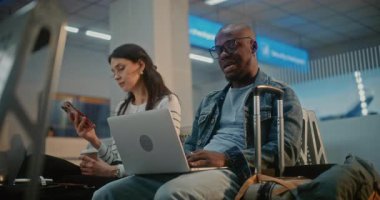 Kalabalık Uluslararası Havaalanı Terminali: Laptop 'ta çalışan Afro-Amerikan Adam, Çevrimiçi Video Görüşmesi Var. Çeşitli İnsanlar, Yolcular, Hava Yolları Merkezinin Kalkış Salonunda, Uçuşu Bekliyorlar..