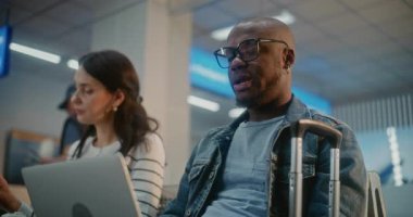 Kalabalık Uluslararası Havaalanı Terminali: Laptop 'ta çalışan Afrikalı Amerikalı Adam, Çevrimiçi Video Sohbeti Var. Çeşitli İnsanlar ve Yolcular, Havayolu Merkezinin Kalkış Salonu 'nda, Uçuşu Bekliyorlar..