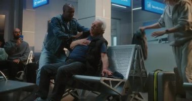 Kalabalık Uluslararası Havalimanı Terminali: Yaşlı Adam Kalp krizi geçiriyor, Infarction in Inarding Lounge of Airline Hub. Kıdemli Yolcuya Yardım Eden Çeşitli İnsanlar, Havaalanı İşçisi Tıbbi Yardım Çağrısı.