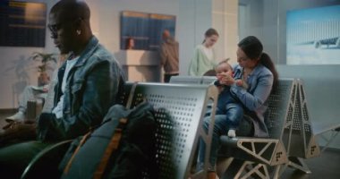 Kalabalık Uluslararası Havaalanı Terminali: Laptop kullanan Afrikalı Amerikalı Adam, Küçük Bebekle Oturan Kadın. Çeşitli Gezginler, Yolcular, Uçak Kalkış Salonunda Uçak Uçuşunu Bekliyor.