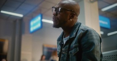 Kalabalık Uluslararası Havalimanı Terminali: Afro-Amerikan Adam Burger Yiyor ve Akıllı Telefon Kullanıyor Havayolu Merkezinin Yatılı Salonunda Oturuyor. Gecikmeli uçuş bekleyen yolcu. Ortalama Yakın Çekim.