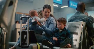 Kalabalık Uluslararası Havaalanı Terminali: Uçak Uçuşunu Bekleyen İki Küçük Çocuğu Olan Anne, Küçük Çocuk Dijital Tablet 'te Çizgi Film İzliyor. Hava Yolları Merkezinin Ayrılış Salonundaki Çeşitli Yolcular.