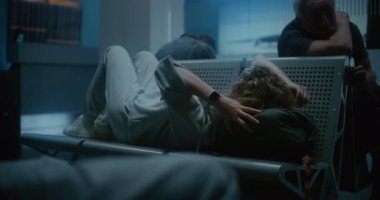 Kalabalık Uluslararası Havalimanı Terminali: Yorgun Bir Kadın Sırt Sırtında Uyuyor Gece Havalimanı İnbotu 'nda. Çeşitli İnsanlar ve Yolcular Gecikmiş Uçak Uçuşunu Bekliyor.