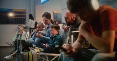 Kalabalık Havaalanı Terminali: Kulaklıklı Genç Çocuk, Akıllı Telefon Kullanıyor, Ailesi ve İki Çocuk Dijital Tablet 'te Çizgi Film İzliyor. Çeşitli Yolcular, Uçak Hanı Biniş Salonunda Uçuşu Bekliyor.