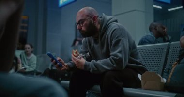 Gece Havalimanı 'nın Kalkış Salonu: İnsan Burger Yiyen ve Kaydıran Telefon Kalabalık Uluslararası Havaalanı Terminalinde Oturuyor. Yorgun İnsanlar ve Yolcular Gecikmiş Uçak Uçuşunu Bekliyor.
