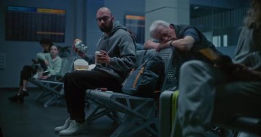 Kalabalık Uluslararası Havaalanı Terminali: Burger Yiyen ve İçen Adam Gece Havalimanı 'nda Oturarak Kahve İçen Adam. Yorgun İnsanlar ve Yolcular Gecikmiş Uçak Uçuşunu Bekliyor.