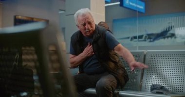 Kalabalık Uluslararası Havaalanı Terminali: Yaşlı Adam Kalp krizi geçiriyor, Acılı Göğsü Sıkışan Hava Yolları Merkezinde Oturuyor. Çeşitli İnsanlar ve Havalimanı Personeli Yaşlı Yolculara Yardım Ediyor.