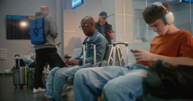 Kalabalık Uluslararası Havalimanı Terminali: Havayolu Merkezinin Gidiş Salonu 'ndaki Çeşitli İnsanlar ve Yolcular. Bilgisayarda çalışan Afro-Amerikalı Adam Otururken ve Uçak Beklerken.