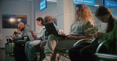 Kalabalık Uluslararası Havalimanı Terminali: Airline Hub 'ın Kalkış Salonu' nda oturan çeşitli yolcular, Uçuşu Bekliyor, Telefonları Kullanıyor. Uzaktan kumandalı dizüstü bilgisayarlar üzerinde çalışan Afrikalı Amerikalı erkek ve kadın..