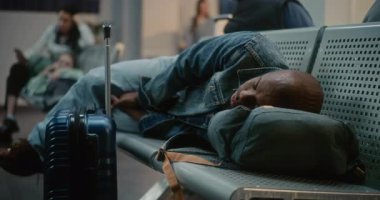 Kalabalık Uluslararası Havaalanı Terminali: Bavul ve Sırt Çantalı Yorgun Afro-Amerikan Turist Yataklı Havayolu Merkezinde Koltuklarda Uyuyor. Çeşitli Yolcular Gecikmeli Uçuş Bekliyor