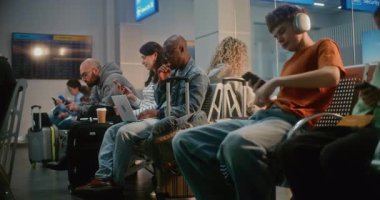 Kalabalık Uluslararası Havalimanı Terminali: Çeşitli İnsanlar, Uçak İnbotu 'nun Ayrılış Salonu' nda oturan Yolcular, Uçak Uçuşunu Beklemek, Telefonları Kullanmak. Bilgisayarda çalışan Afrikalı Amerikalı Adam.