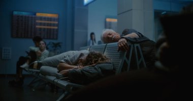 Kalabalık Uluslararası Havalimanı Terminali: Tablet Bilgisayar kullanan yorgun ve uykulu adam, Geceleri Havayolu İnbotu 'nun Yatılı Salonunda Koltuklarda Uyuyan Kadın. Çeşitli Yolcular Gecikmeli Uçuş Bekliyor.