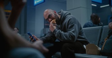 Gece Havalimanı 'nın Kalkış Salonu: İnsan Burger Yiyen ve Kaydıran Telefon Kalabalık Uluslararası Havaalanı Terminalinde Oturuyor. Yorgun İnsanlar ve Yolcular Gecikmiş Uçak Uçuşunu Bekliyor.